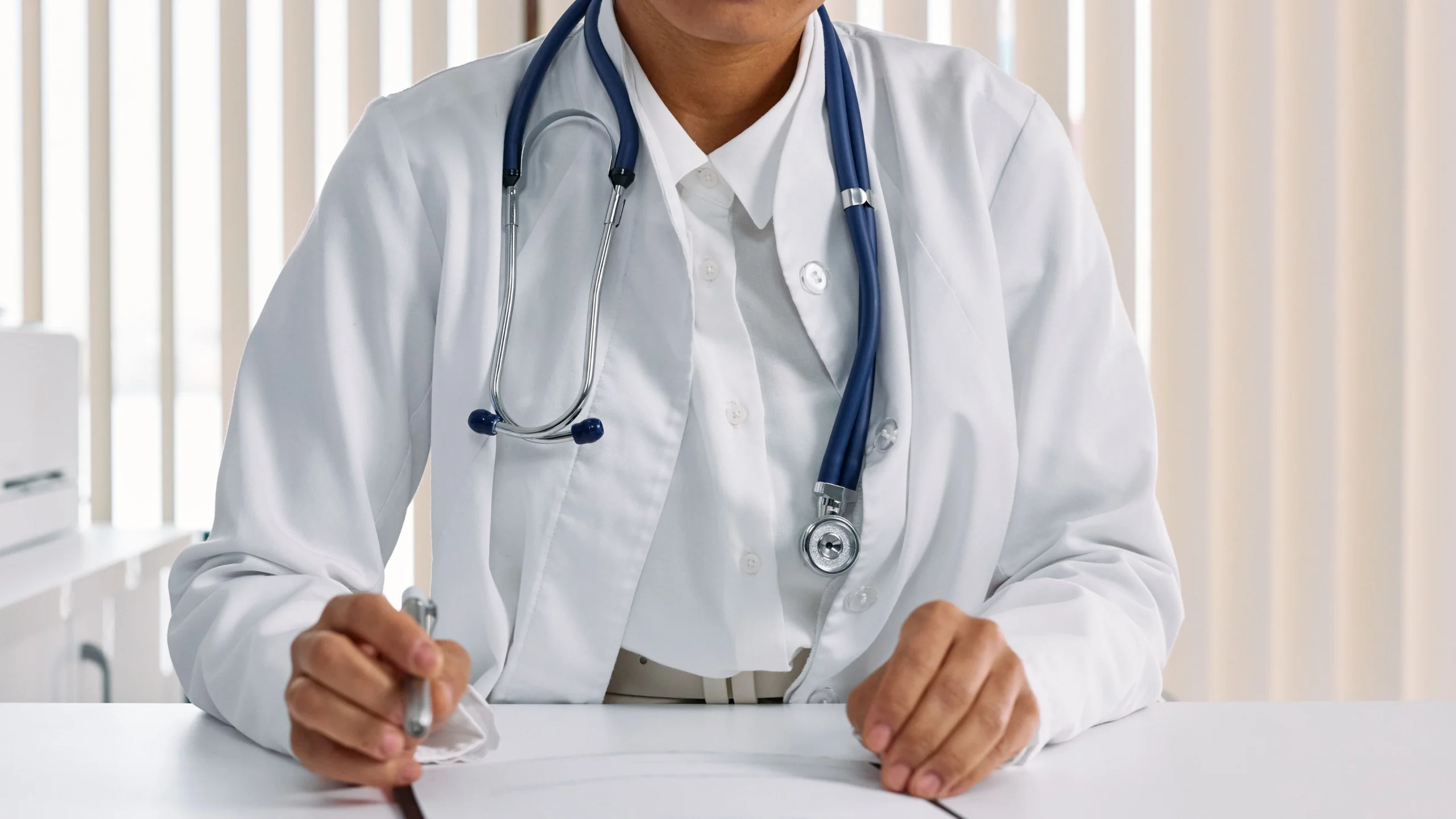 Physician in a white coat with a stethoscope reviewing claim paperwork at a desk