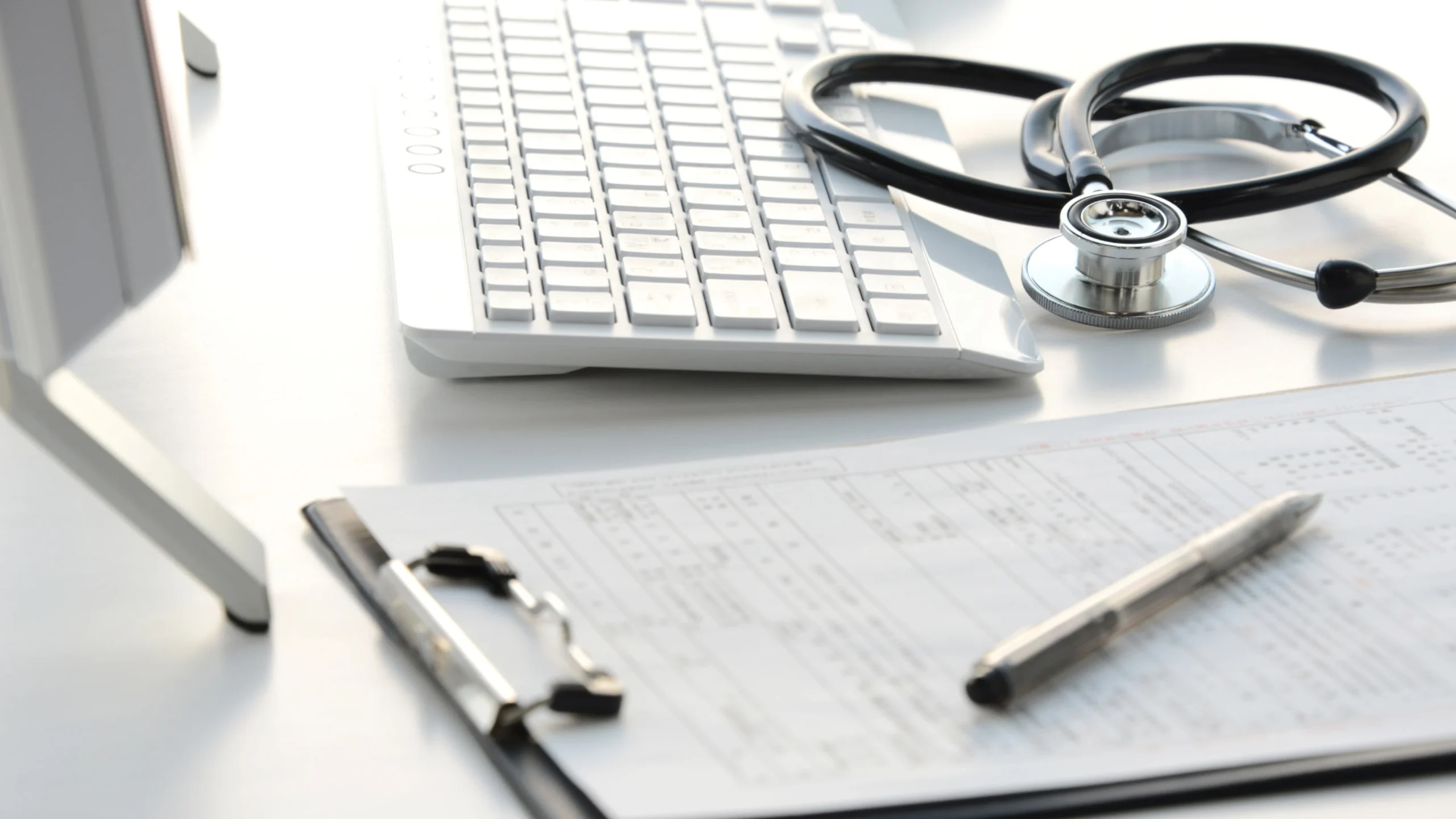 Medical claim form on a clipboard beside a keyboard and stethoscope on a desk