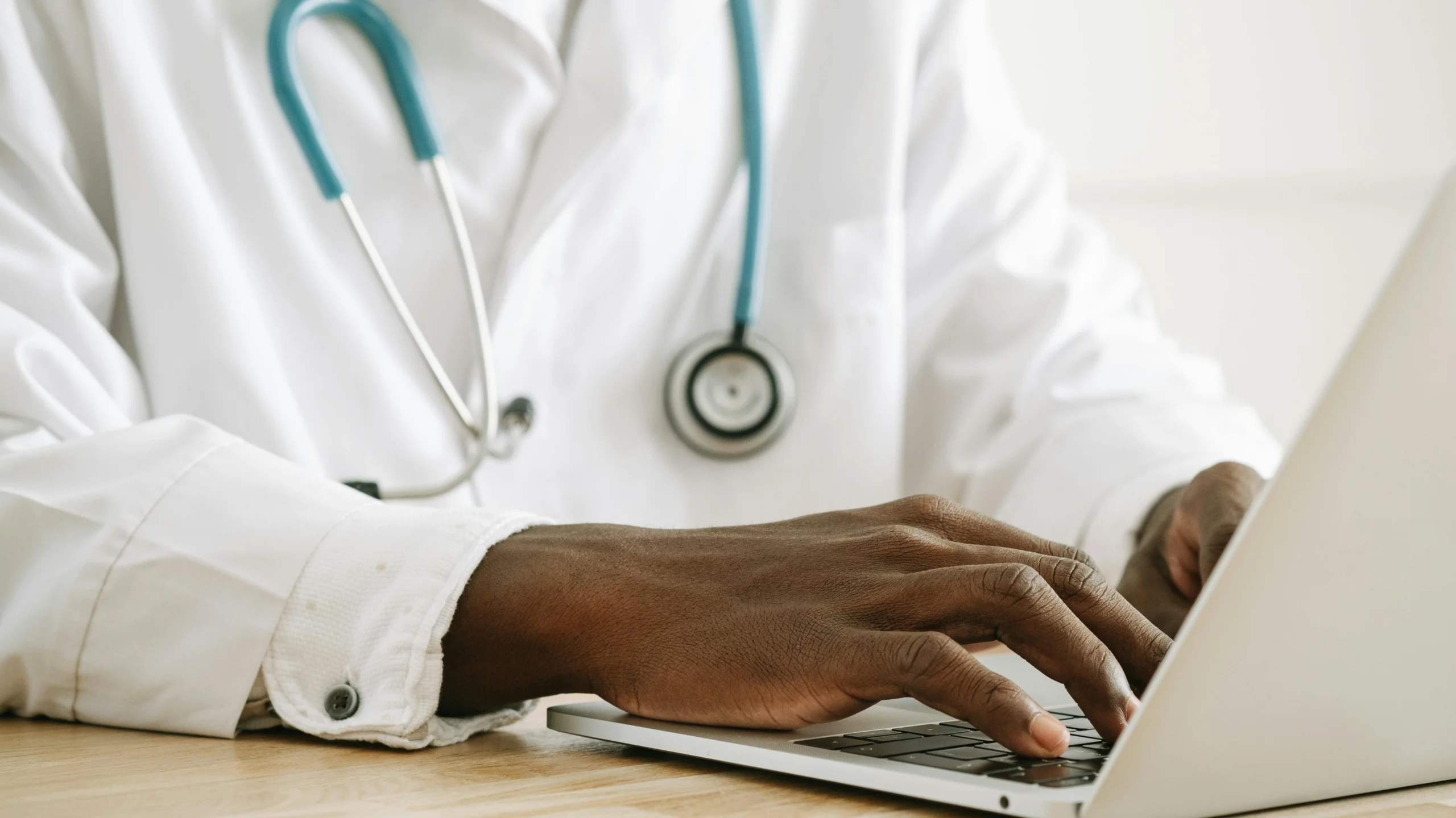 Clinician in a white coat with a stethoscope working at a laptop